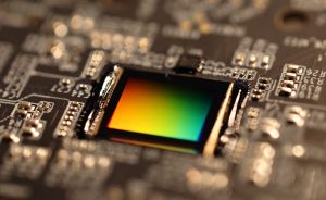 Nahaufnahme einer Leiterplatte mit einem quadratischen Bildsensor, der ein regenbogenfarbenes Schillern zeigt.